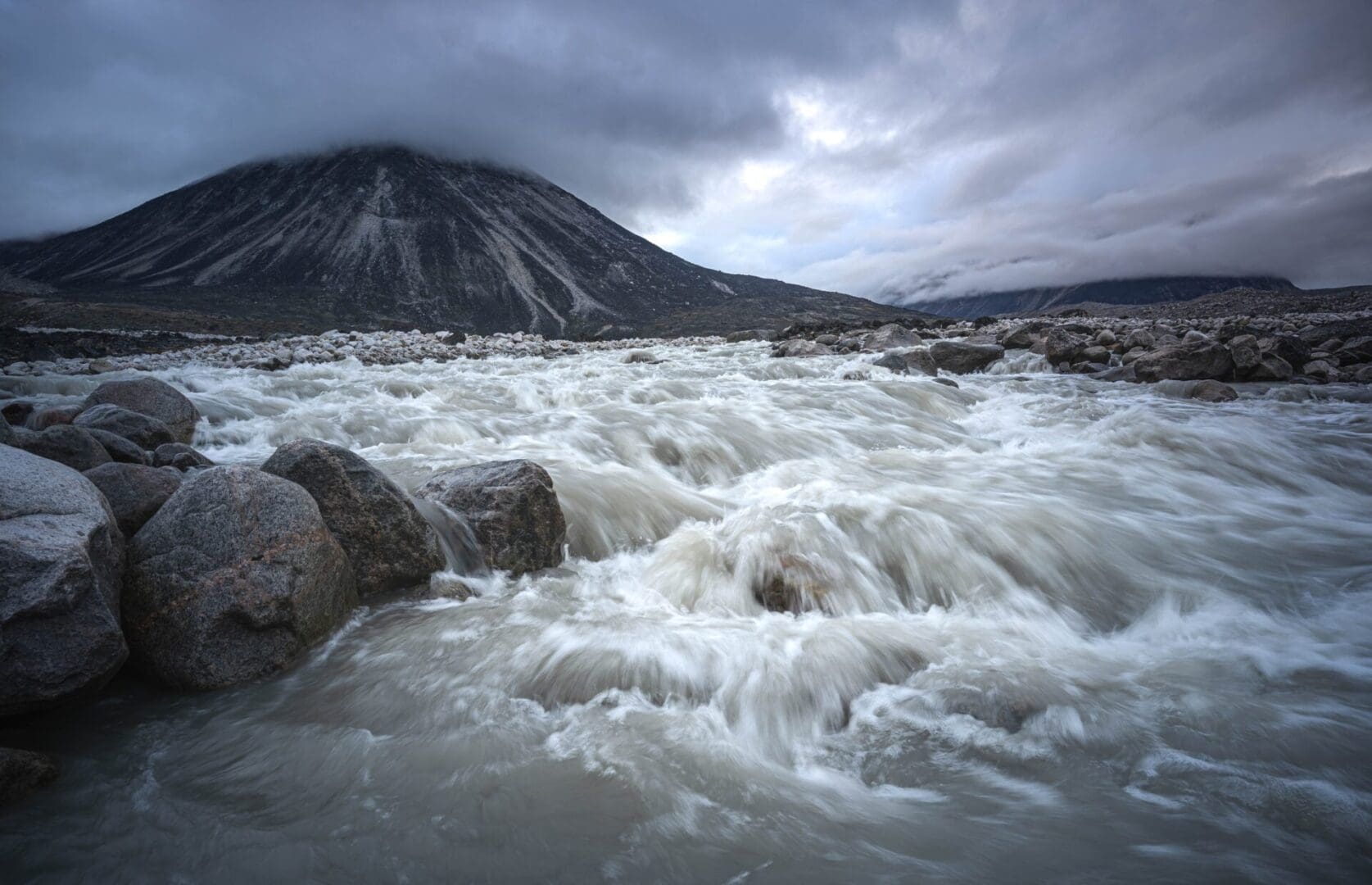 Fast-flowing river with rocks and mountain.